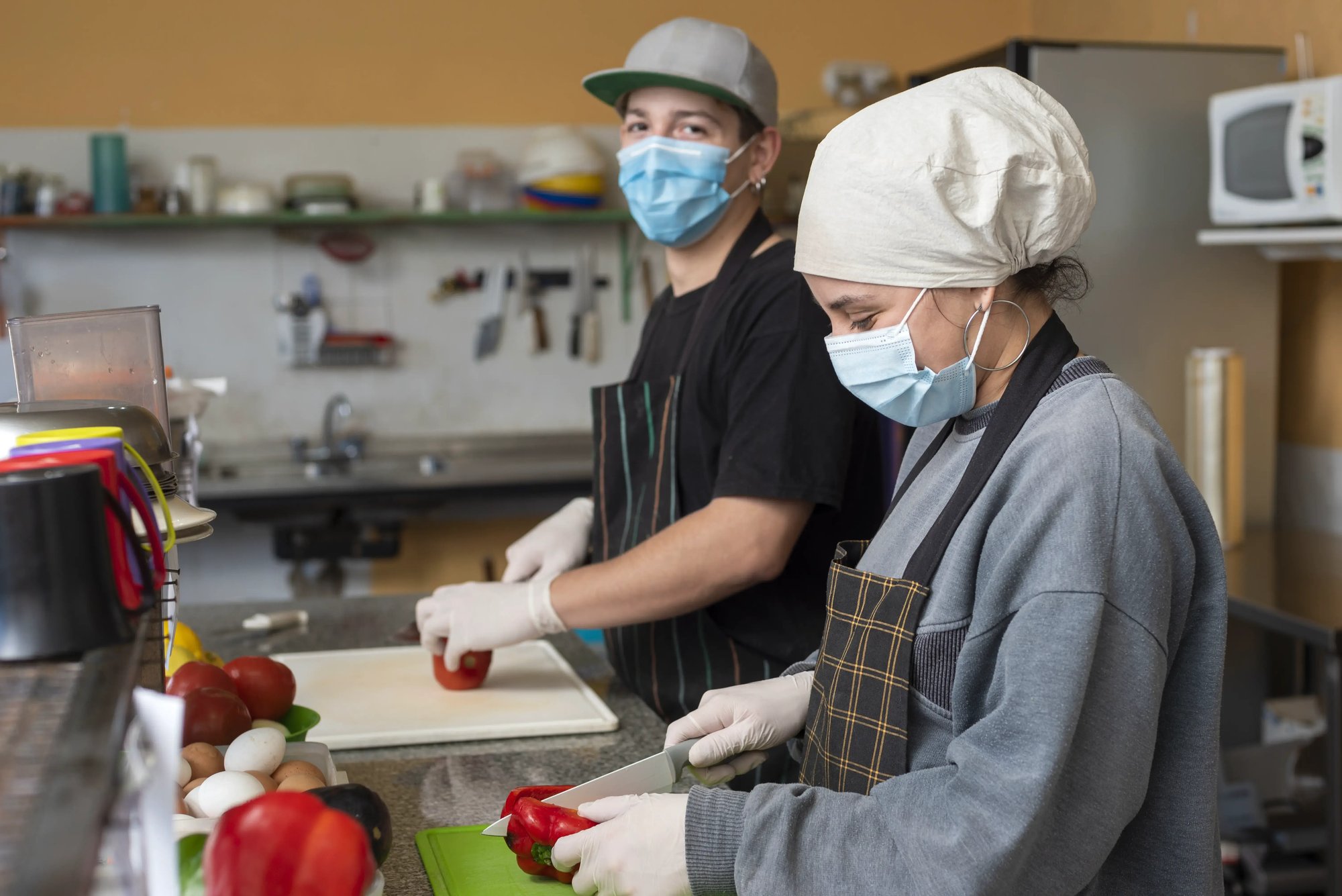 two-young-chefs-slicing-vegetables-wearing-medical-masks
